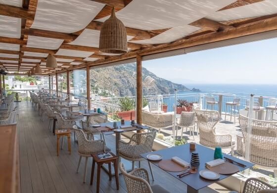 Area pranzo all'aperto con vista sul mare e tavoli apparecchiati.