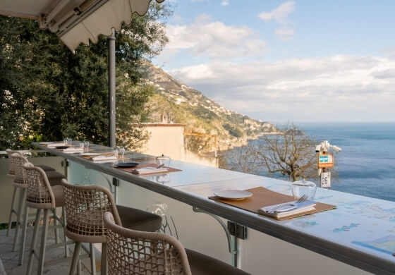 Area pranzo all'aperto con vista mare e città costiera.