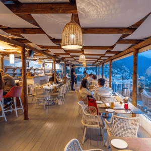 Open-air restaurant with woven lights and coastal town view.