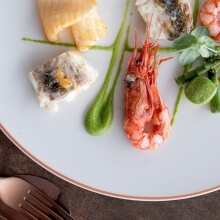 Piatto bianco con bordo rosa oro, pesce, gambero e salsa verde.