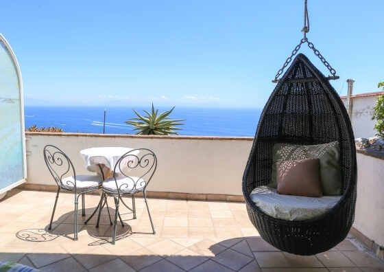 Balcone con tavolo rotondo, sedie, e sedia sospesa, vista sull'acqua.