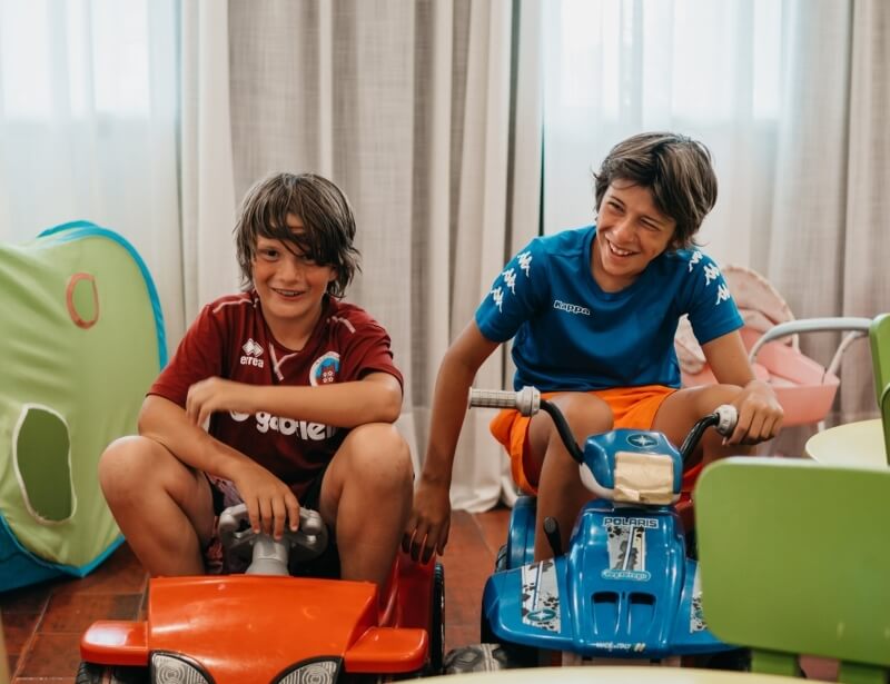 Due ragazzi su veicoli giocattolo, uno rosso e uno blu.