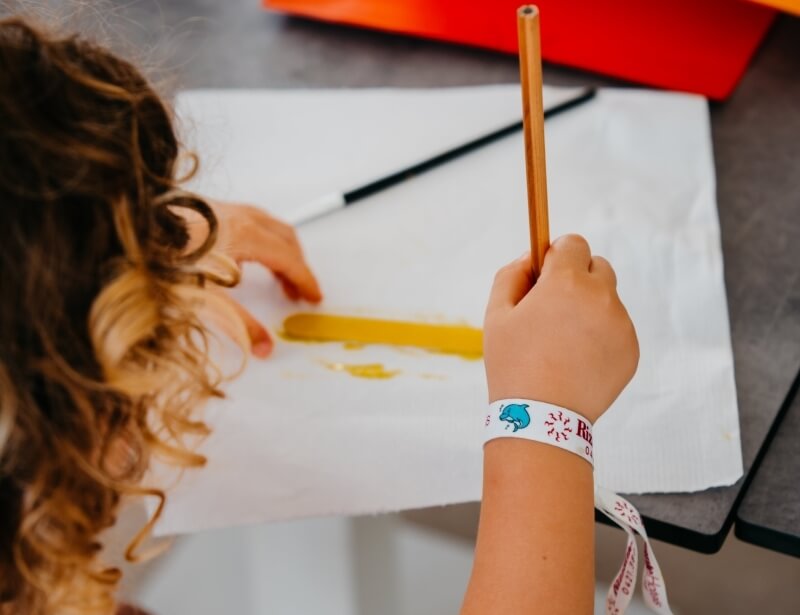 Braccio di bambino con braccialetto bianco e matita su superficie bianca.