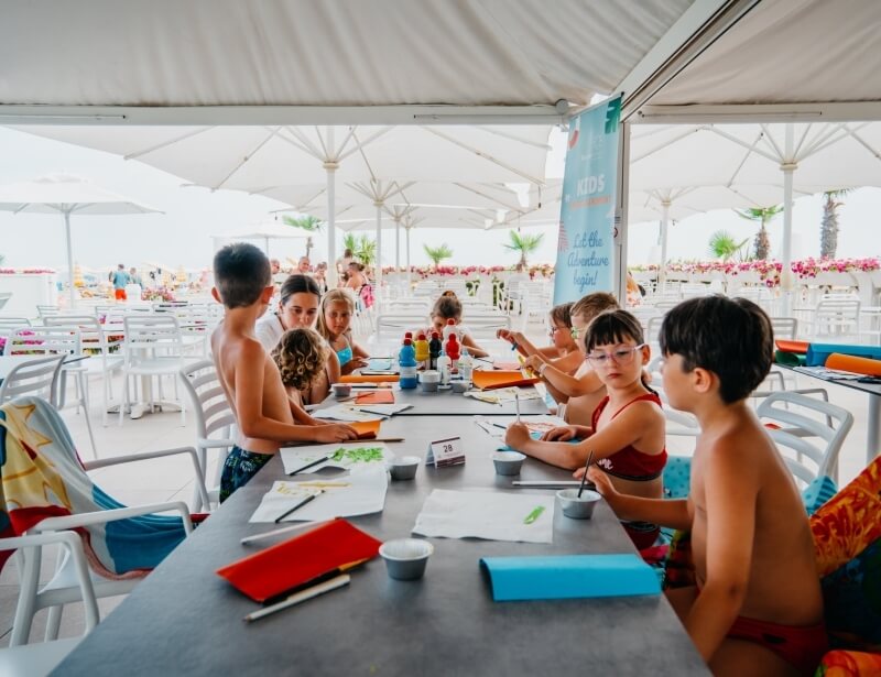 Bambini all'aperto fanno attività artistiche con colori e pennelli.