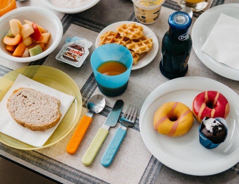 Breakfast spread with fruit, waffles, donuts, and colorful utensils.