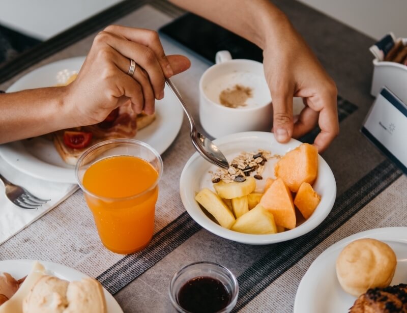 Breakfast spread with juice, yogurt, fruit, pastries, and coffee.
