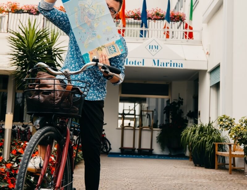 Person in floral shirt with bicycle and map outside Hotel Marina.