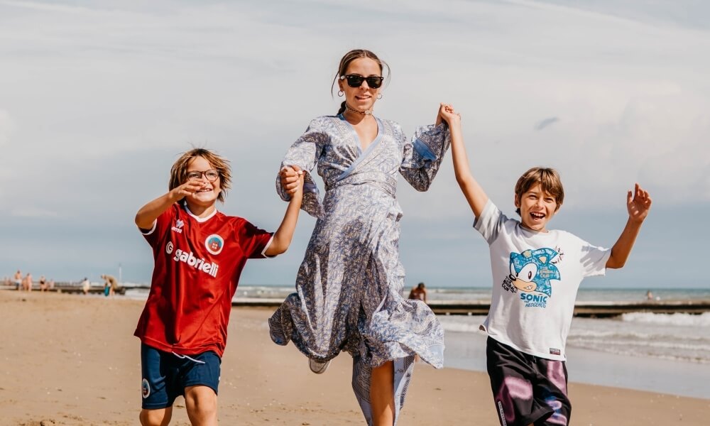 Tre persone sulla spiaggia con nuvole, acqua e struttura in legno.