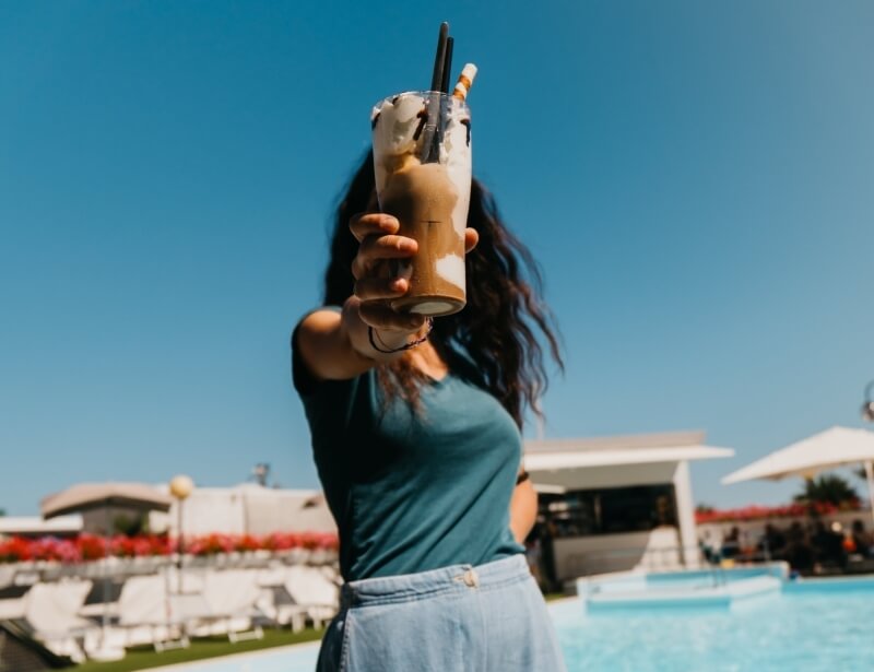 Person holding a tall drink with whipped cream against a blue sky.