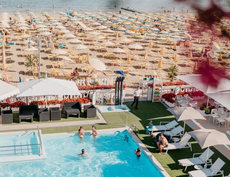 Resort with pool, beach umbrellas, loungers, and people enjoying the sun.