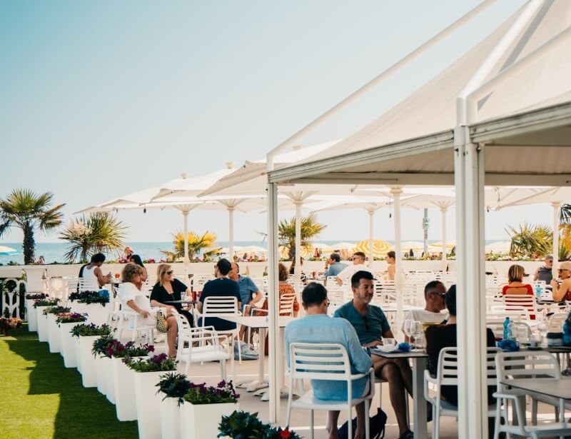 Outdoor seating area with tables, palm trees, and ocean view.