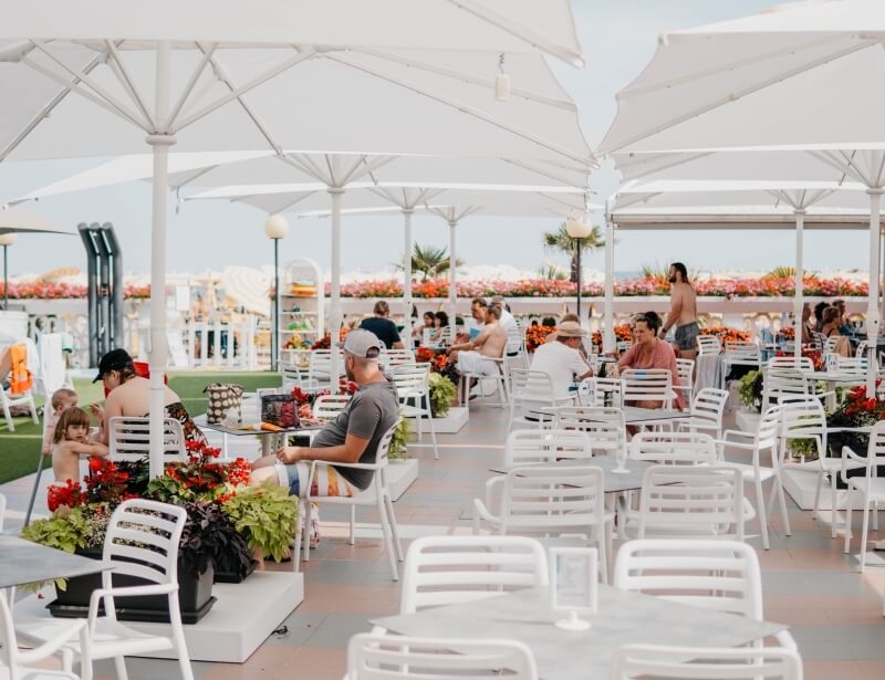 Outdoor seating area with tables, umbrellas, plants, and a playground.