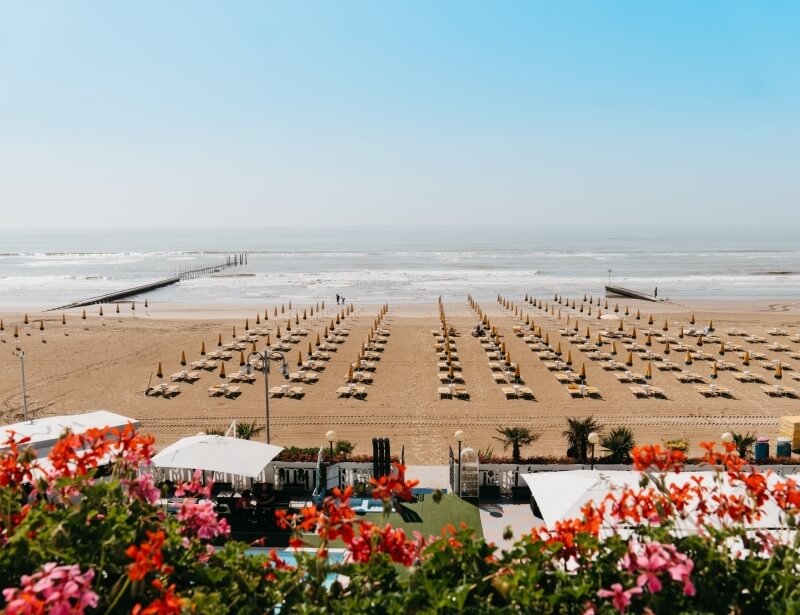 Lounge chairs and umbrellas on a sandy beach with a pier.