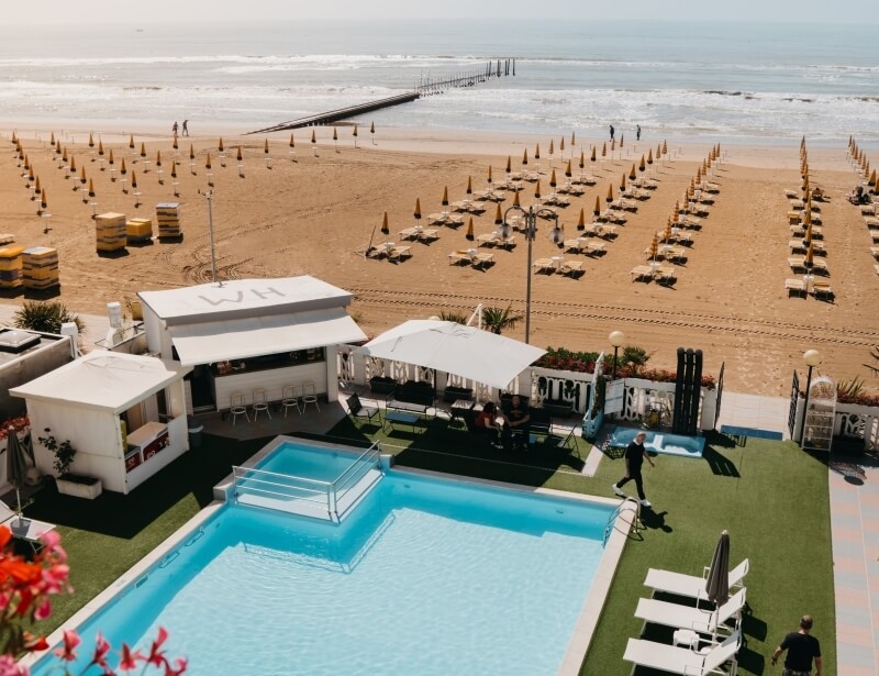 Aerial view of a beach resort with lounge chairs, umbrellas, and a pool.