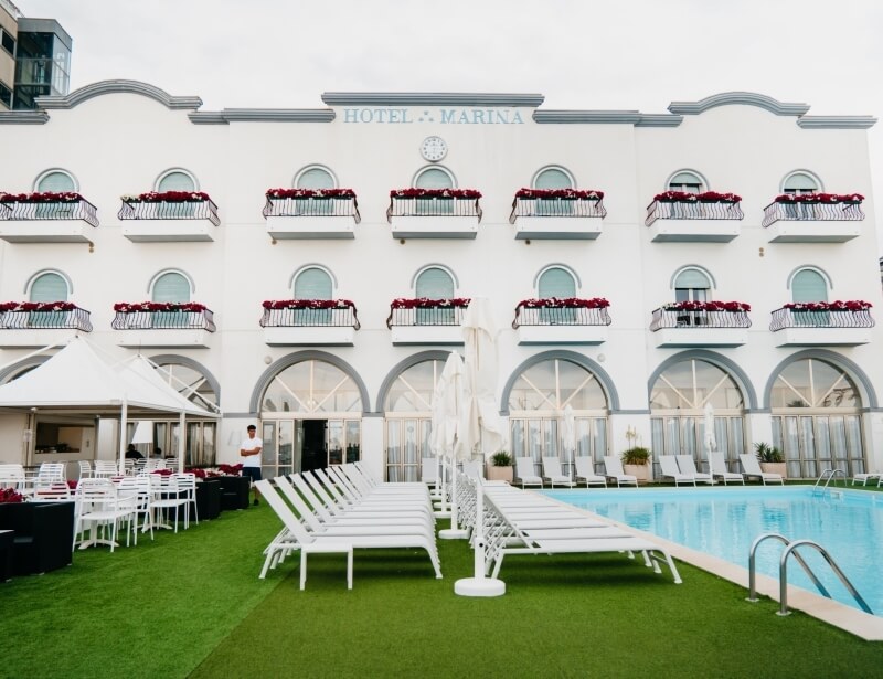 Exterior of HOTEL MARINA with pool, seating area, and flowers.