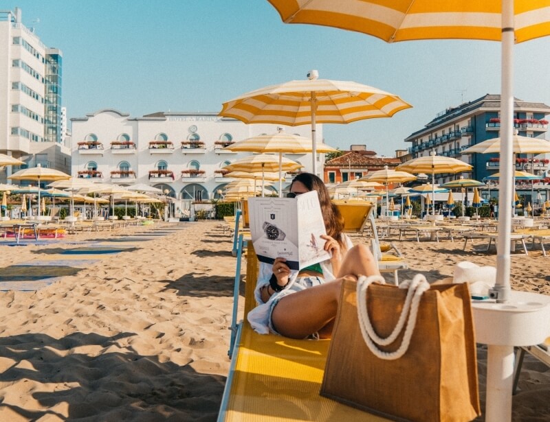 Person reading on a yellow lounge chair at a beach.