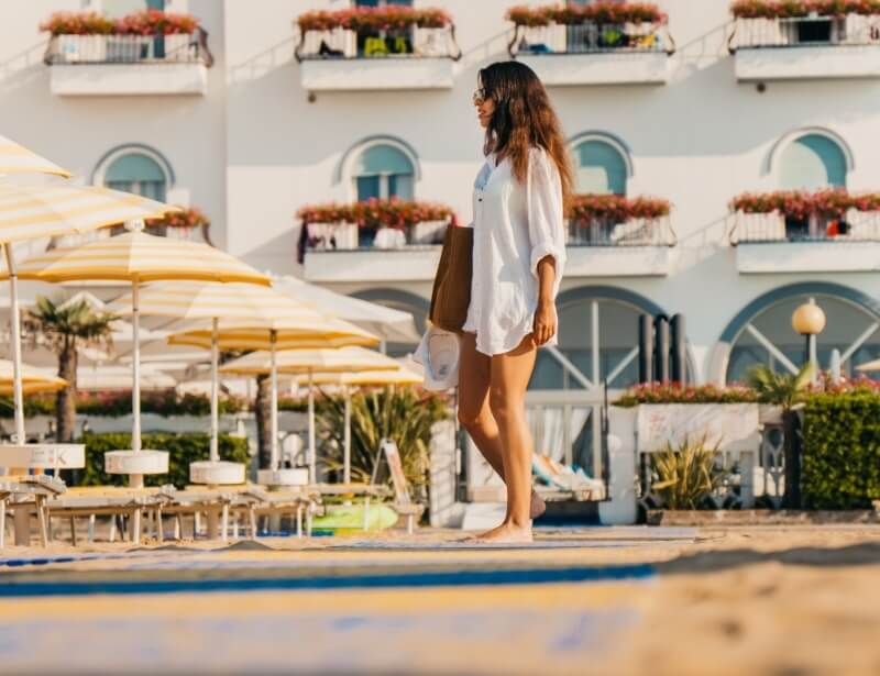 Woman walking on a beach with a white building and umbrellas.