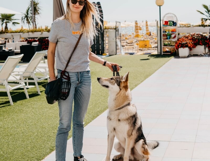Donna con occhiali e cane in spiaggia, sedie e ombrelloni.