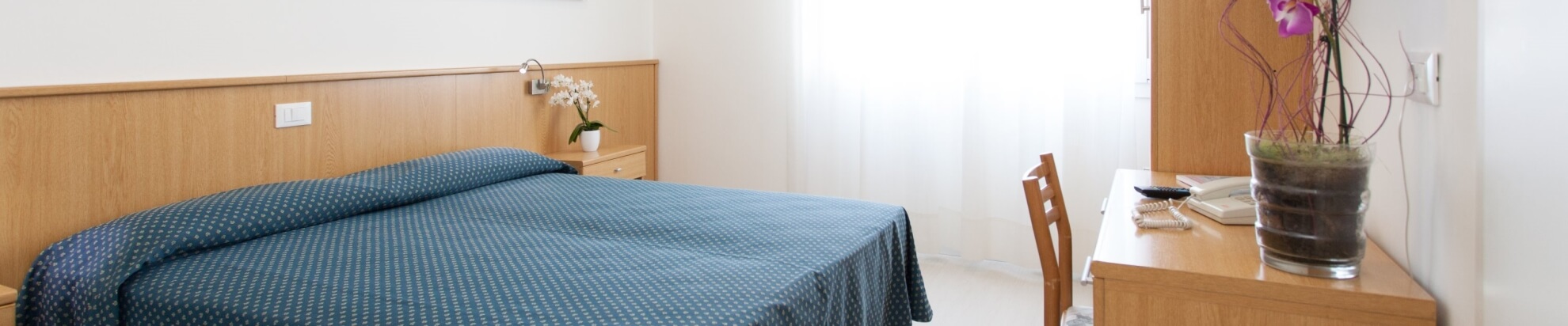 Camera d'hotel con letto, tavolo, lampada e orchidee.