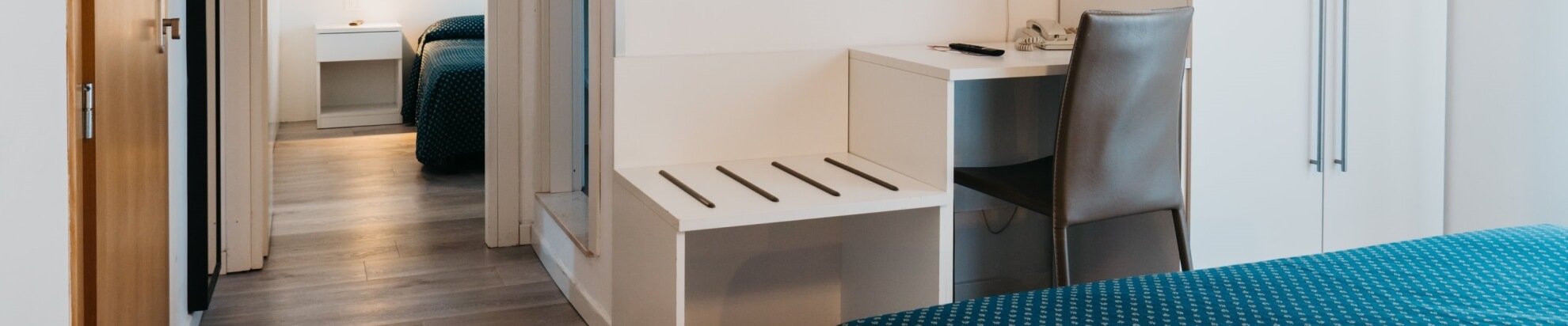 Camera d'hotel con letto, scrivania e armadio visibile.