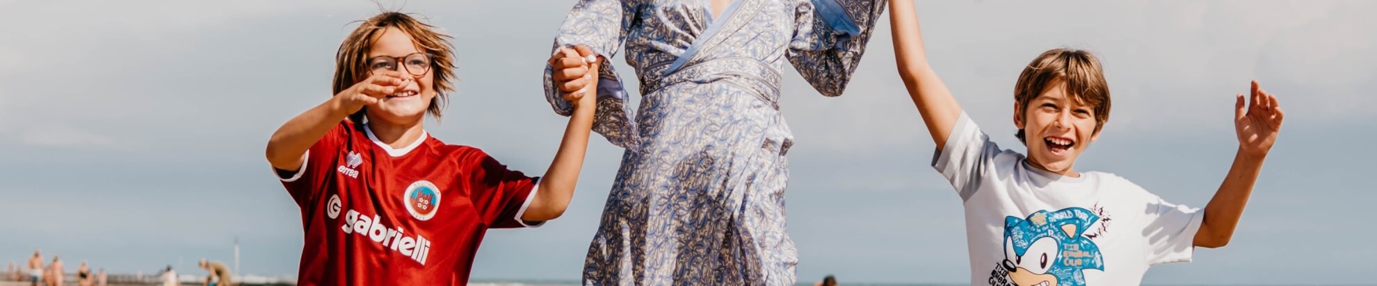 Three people jump hand in hand on a beach.