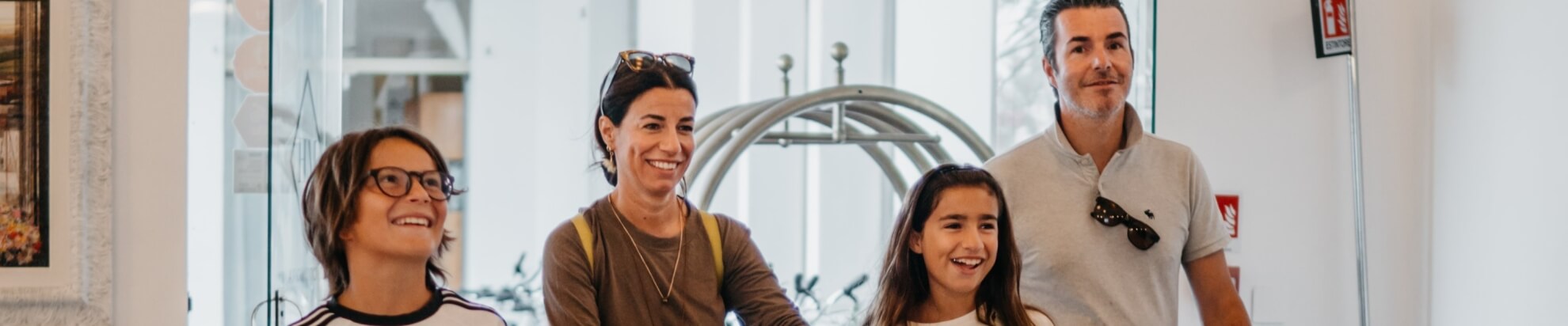 Family of four in hotel lobby with luggage cart and fire extinguisher sign.