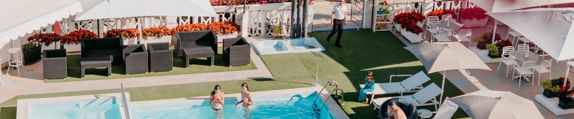 Area esterna con piscina, lettini, piante e persone che si rilassano.