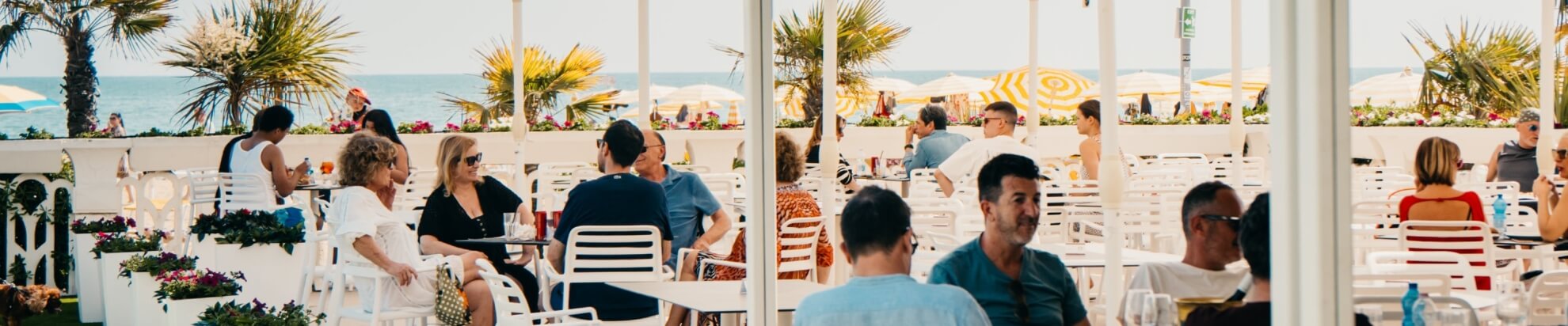 Outdoor dining area with white furniture, palm trees, and ocean view.