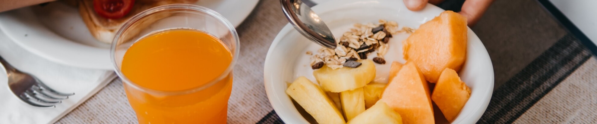 Un bicchiere di succo d'arancia accanto a una ciotola di frutta e granola.