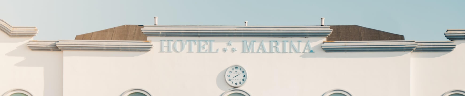 Facciata di un hotel con "HOTEL MARINA" e orologio rotondo.
