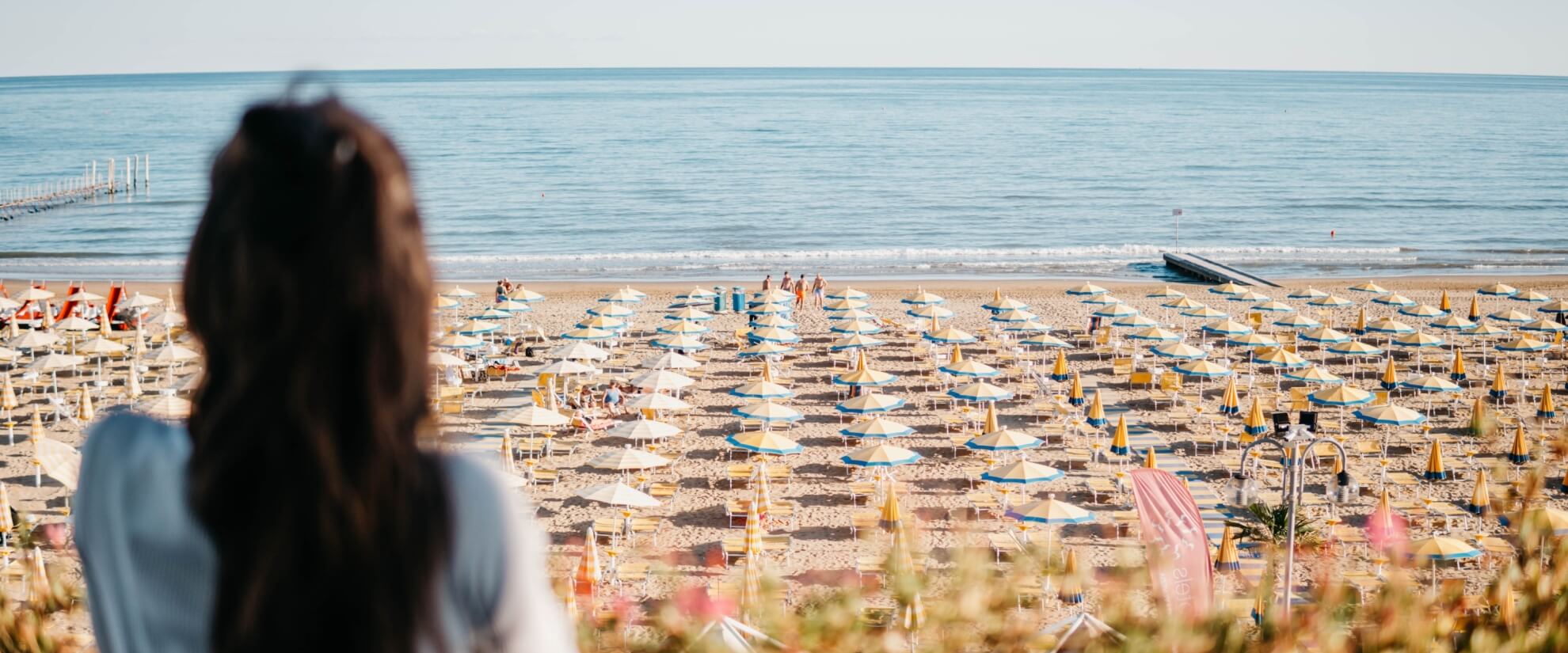 Empty beach with yellow and blue umbrellas, ocean, and blurred figure.