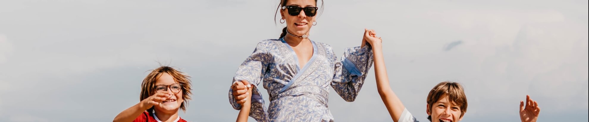 Donna con occhiali da sole e vestito a righe, mano nella mano con due bambini.