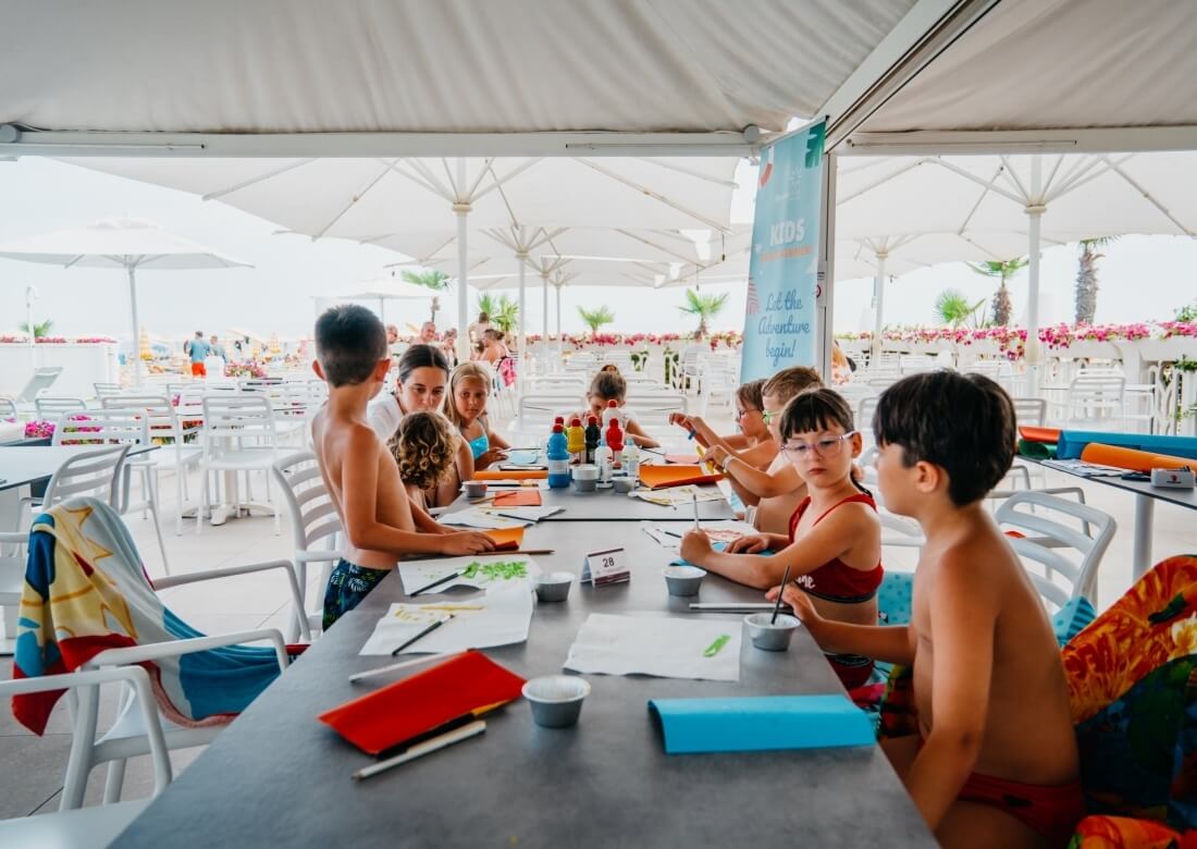Bambini disegnano a un tavolo con materiali artistici all'aperto.