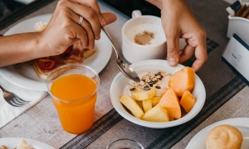 Breakfast table with toast, yogurt, orange drink, and beverage.