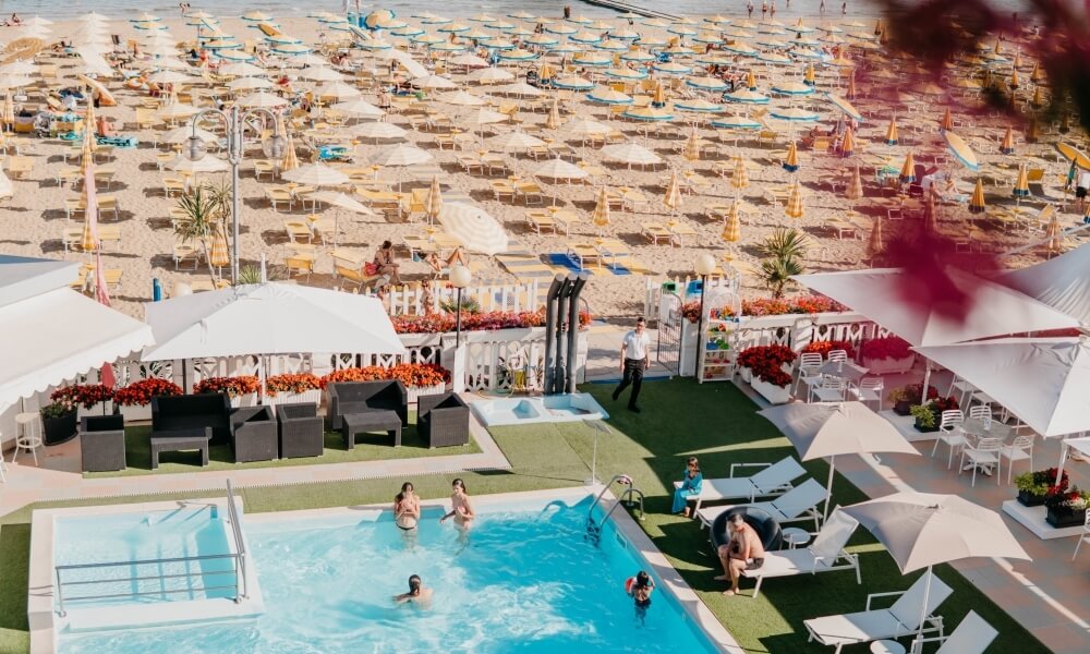 Resort beach with pool, umbrellas, and lounge chairs.
Resort sulla spiaggia con piscina, ombrelloni e lettini.