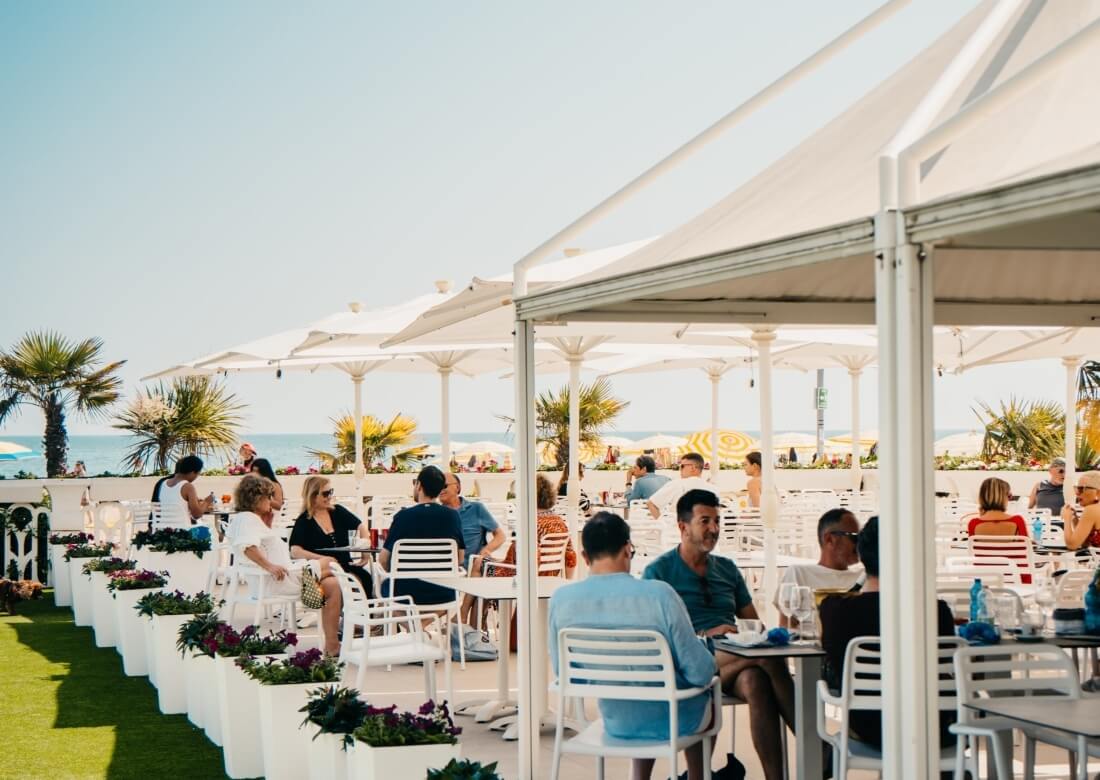 Outdoor seating area with umbrellas, palm trees, and ocean view.