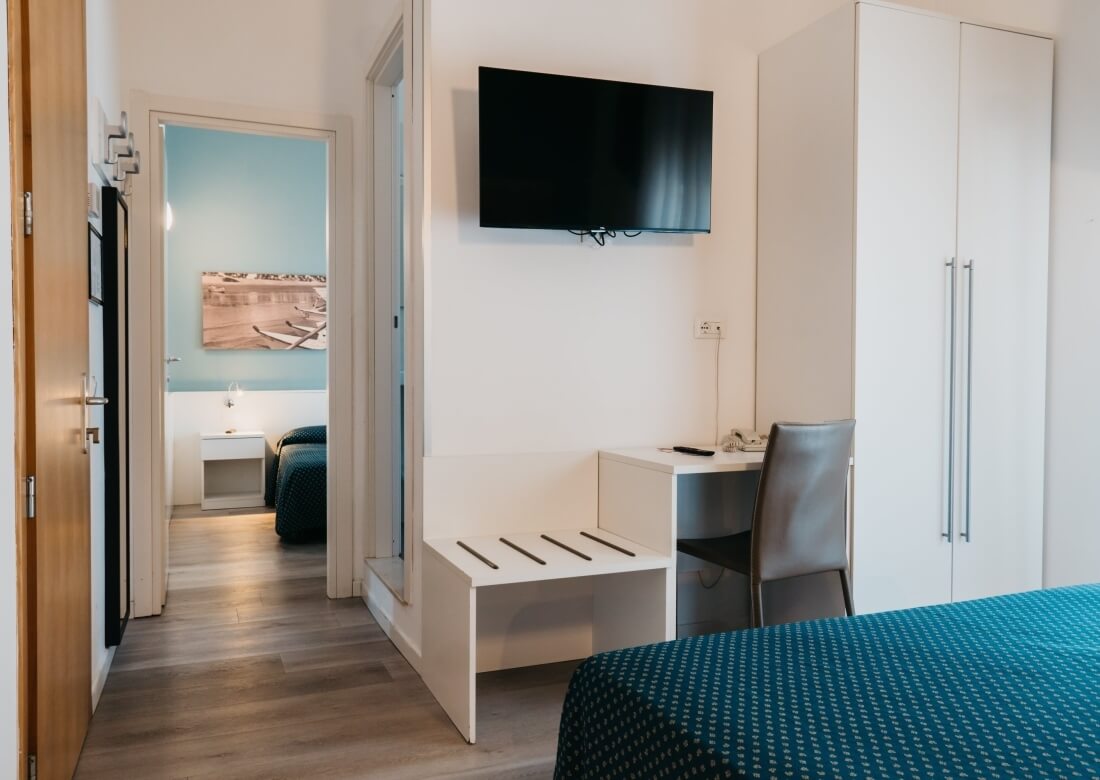 Camera d'hotel con letto, scrivania e armadio visibili.