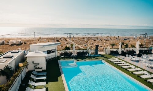 Vista aerea di una piscina blu, spiaggia sabbiosa e oceano.