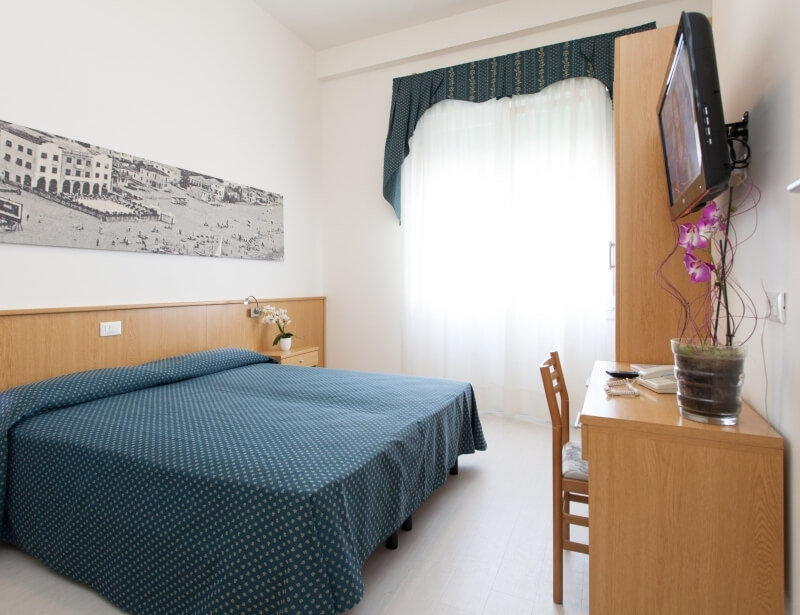 Camera d'hotel con letto, scrivania, TV e decorazioni marine.