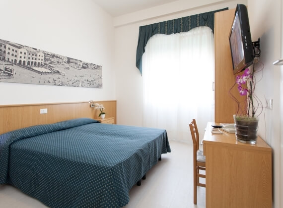 Camera d'hotel con letto, scrivania, TV e finestra.