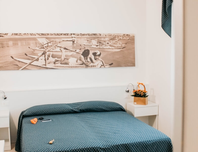 Camera d'hotel con letto, comodini bianchi e quadro di spiaggia.