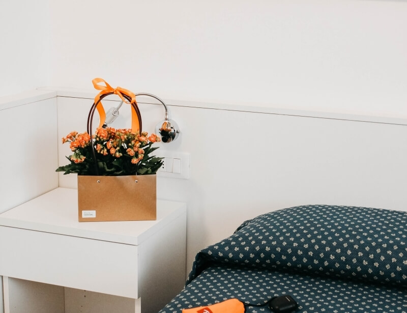 Letto con coperta blu, comodino con fiori arancioni e lampada.