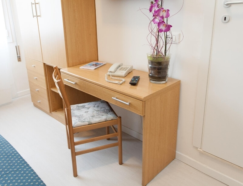 Holztisch mit Telefon, Vase, Stuhl und Schrank; weißer Boden.