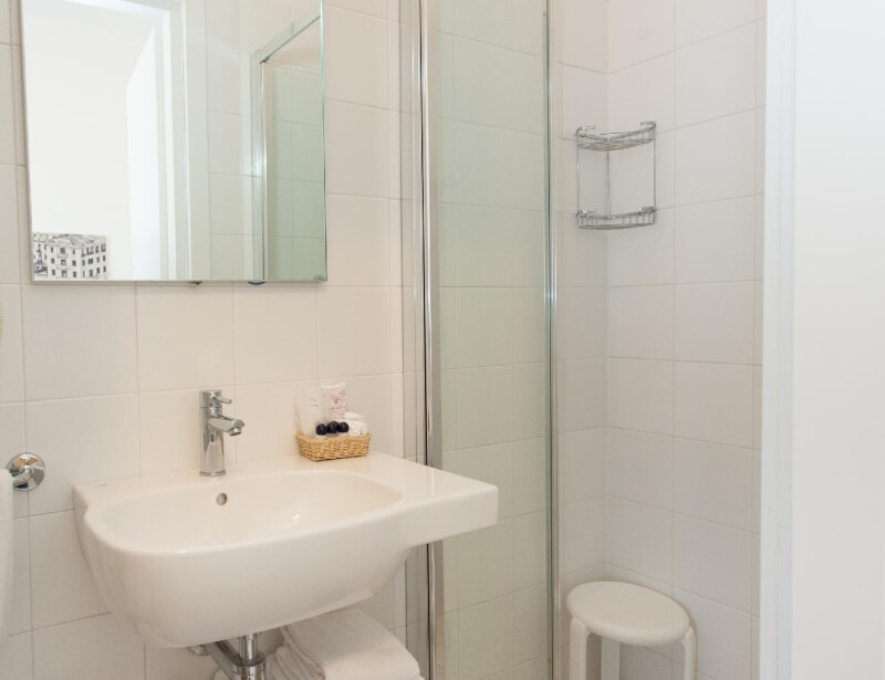 Badezimmer mit Waschbecken, Spiegel, Duschkabine und Toilettenartikeln.