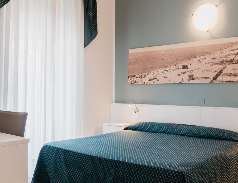 Camera d'hotel con letto teal, foto panoramica e scrivania.