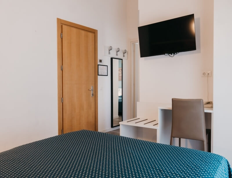 Camera d'hotel con letto, scrivania, TV e specchio.