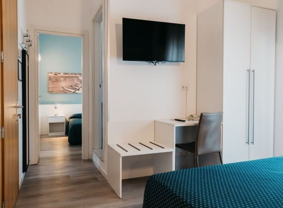 Camera d'hotel con TV, scrivania, sedia e armadio bianco.