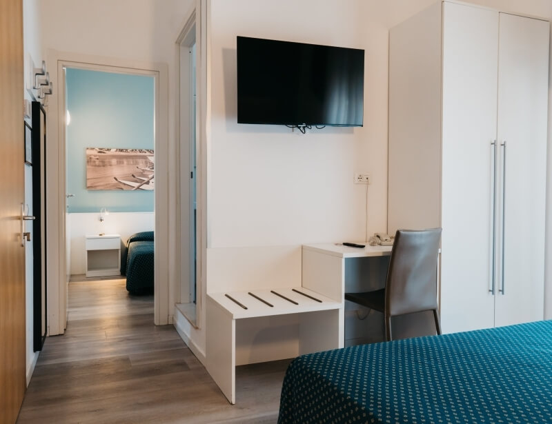 Camera d'hotel con letto, scrivania, armadio e porta aperta.