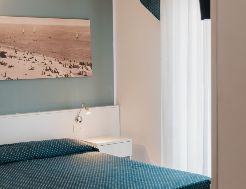 Camera d'hotel con letto, coperta turchese e quadro di spiaggia.