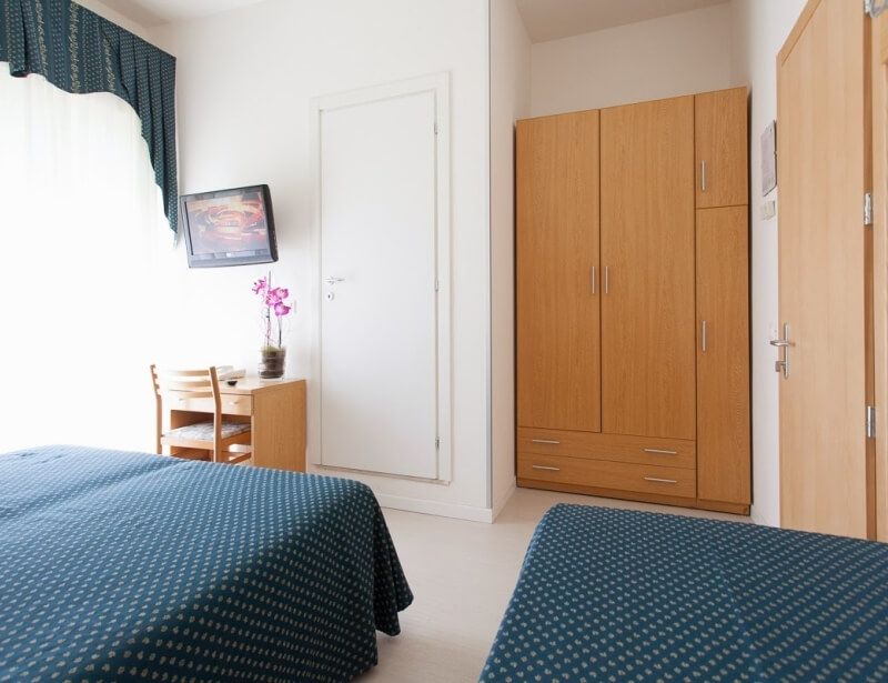 Camera d'hotel con due letti, scrivania e armadio in legno.